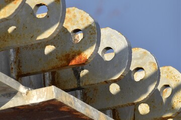 Repeating pattern of a row of metal flanges with holes, with patterns of shadows.