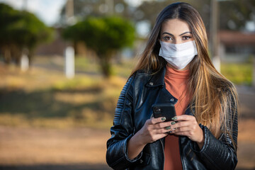 Latin american woman using cell phone wearing face protection mask as prevention for coronavirus. Use of COVID-19 mask required in the city. Corona virus.