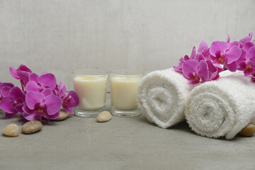 Obraz na płótnie Canvas branch pink orchid flower with two rolled towel and white candle,stones on gray background