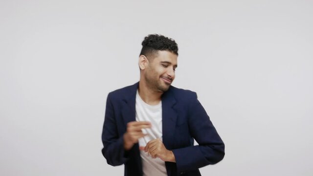 Positive bearded man in suit having fun dancing and moving to rhythm, dabbing raising hands, making dubdance gesture. Indoor studio shot isolated on gray background