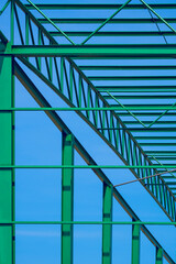 Green steel roof of warehouse building structure in construction area against blue sky background in vertical frame