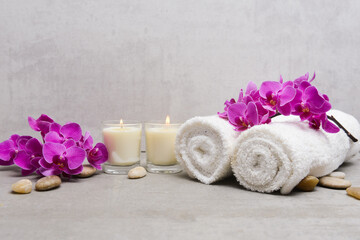 branch pink orchid flower with rolled towel and white candle,stones on gray background