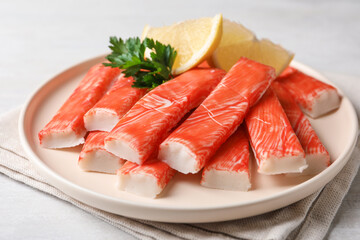 Plate of fresh crab sticks with lemon on white table, closeup