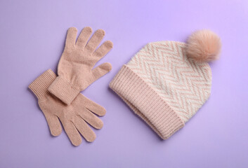 Woolen gloves and hat on violet background, flat lay