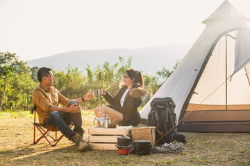 man and woman sitting in chairs outside the tent. Couple camping in forest. Friends Camping Eating...