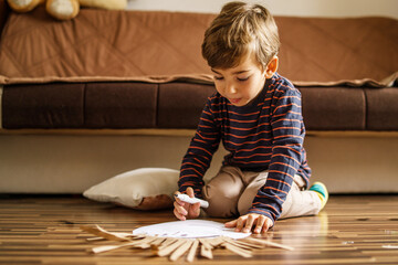 Small caucasian boy playing on the floor at home using crayon to draw on the paper toy homemade art developing new skill - leisure activity playful kid growing up concept