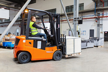 Storehouse employee in uniform working on forklift in modern automatic warehouse. Boxes are on the...