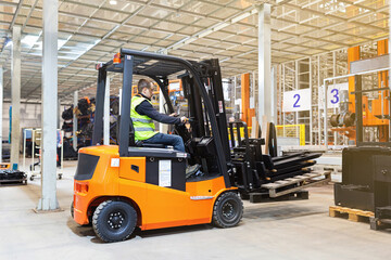 Fototapeta na wymiar Storehouse employee in uniform working on forklift in modern automatic warehouse. Boxes are on the shelves of the warehouse. Warehousing, machinery concept. Logistics in stock.