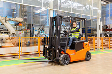 Storehouse employee in uniform working on forklift in modern automatic warehouse. Boxes are on the shelves of the warehouse. Warehousing, machinery concept. Logistics in stock. - Powered by Adobe