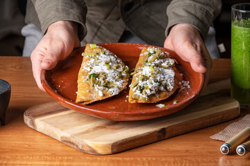 A man serving a mexican dish of quesadillas with white cheese and nopales in a wooden table