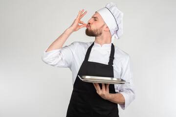 Chef man. Portrait of chef cook showing empty tray. Cook shows something very tasty. Chef makes gesture deliciously with his hands. Cooking satisfied cook on gray background. New recipe appreciation