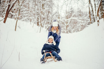 Fototapeta na wymiar Beautiful mother in a blue jacket. Family sledding in a winter park. Little boy in a cute hat