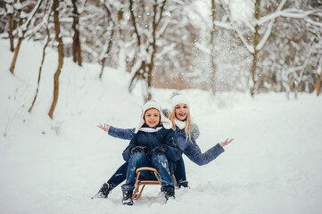 Fototapeta premium Beautiful mother in a blue jacket. Family sledding in a winter park. Little boy in a cute hat