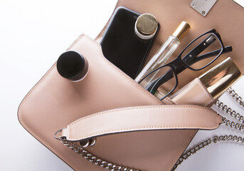 Makeup products and mobile in trendy handbag on white background. Close up.