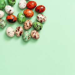 Colorful small quail eggs on light green. Top view spring Easter holiday background