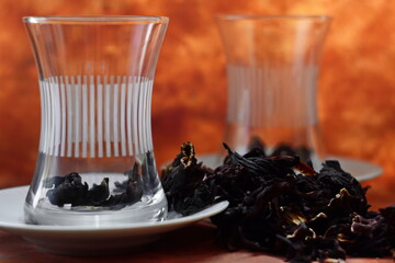pair of transparent empty traditional Turkish glass teacups with fruit dried peel of pomegranate around on brown background. Selective focus on first cup