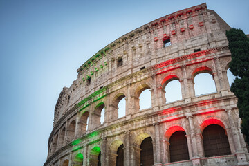 Fototapeta na wymiar The famous Colosseum in Rome illuminated in Italian flag tricolore at twilight