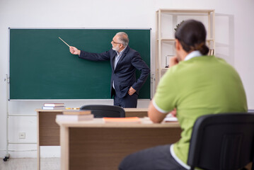 Aged teacher and young male student in the classroom