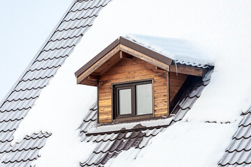 close-up of a mansard plastic window on a country house, the roof is covered with snow