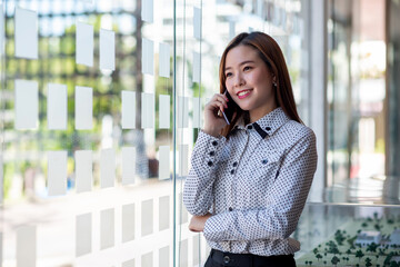 Fototapeta premium Attractive young asian business woman standing talking on the mobile phone in the office.
