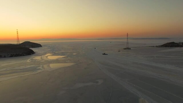 Drone view of the ice-bound strait with tugboats operating at sunset