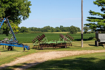 Landscape view of vintage farm implements, including a sprayer, disc cultivator, and a grain trailer