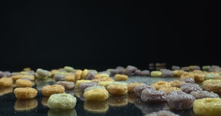 Colorful Cereal Hoops reflect on a glossy black surface. Healthy multicolored cereal on black background. Food concept.