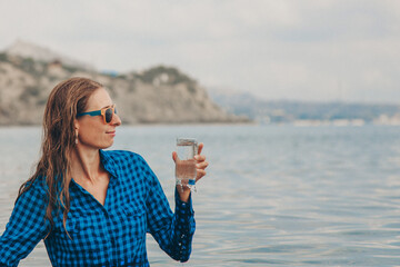 a happy girl sits in the river and drinks water from a glass. Concept of clean natural sources, environmental protection