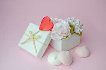 Gift box with flowers and meringues on a pink background.