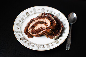 Swiss sponge cake with cream and chocolate on a white plate with a teaspoon.