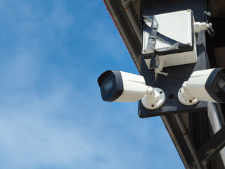 Old CCTV is installed under the building balcony against blue sky.