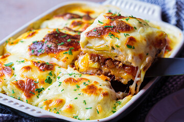 Traditional Greek moussaka - potato and meat casserole with cheese in black oven dish, dark...