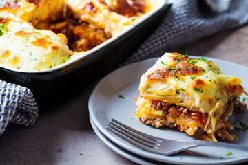Portion of  Greek potato and meat casserole with cheese - moussaka on gray plate, dark background....