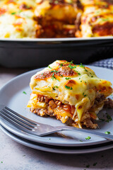 Portion of  Greek potato and meat casserole with cheese - moussaka on gray plate, dark background. Greek food concept.