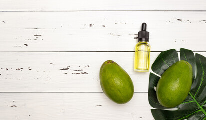 Glass bottle with pipette and avocado oil and avocado fruit on a light wooden background, top view, free space for text. Face and body skin care and healthy nutrition.