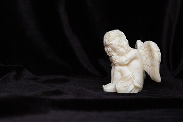 Small angel with wings on a black background, free space for text. Concept of memory of a person,...