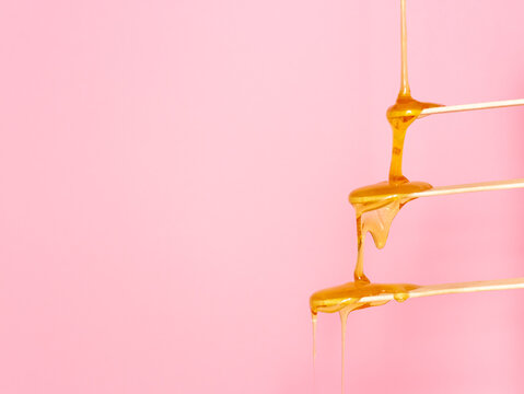 Sugar paste for hair removal runs down a wooden spatula. The concept of depilation, waxing and sugaring. Pink background, free space for text.