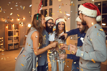 Man pours champagne into glasses to his friends at a New Year's party under the chimes.