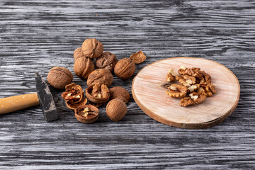 Small hammer, whole and peeled walnuts on a black wooden table.