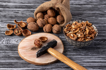Small hammer, little bag, whole and peeled walnuts on a black wooden table.