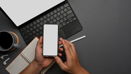 Male hand using smartphone while working with tablet and stationery on the table
