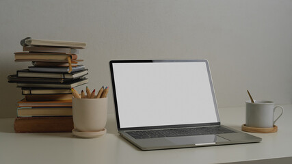 Workspace with laptop, notebook, stack of books and vase in home office room