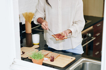 Cropped image of young woman making jelly sandwich for breakfast using wholemeal bread