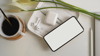 Top view of white table with smartphone, earphone, coffee cup and decorations