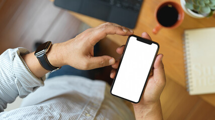Top view of male hands using smartphone on wooden worktable with office supplies