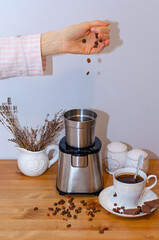Electric coffee grinder grinding coffee beans and standing on the kitchen table, a Cup of black coffee with spices - red pepper and cloves. Morning coffee ritual.