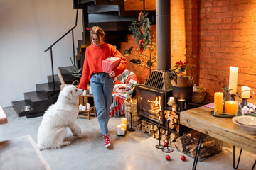 Young woman with her cute dog preparing for a New Year holidays by the fireplace and dining table at home
