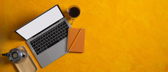 Top view of yellow table with laptop notebook, coffee pot, cup and copy space