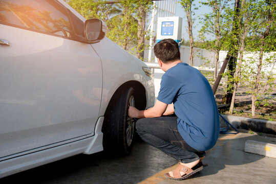 An Asian man inflates tires at a gas station And he is looking at the dial of the auto inflator to check the pressure level.