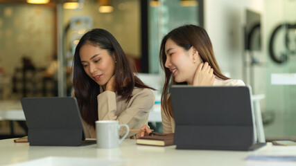 Two female office workers consulting on their project with digital tablets in meeting room